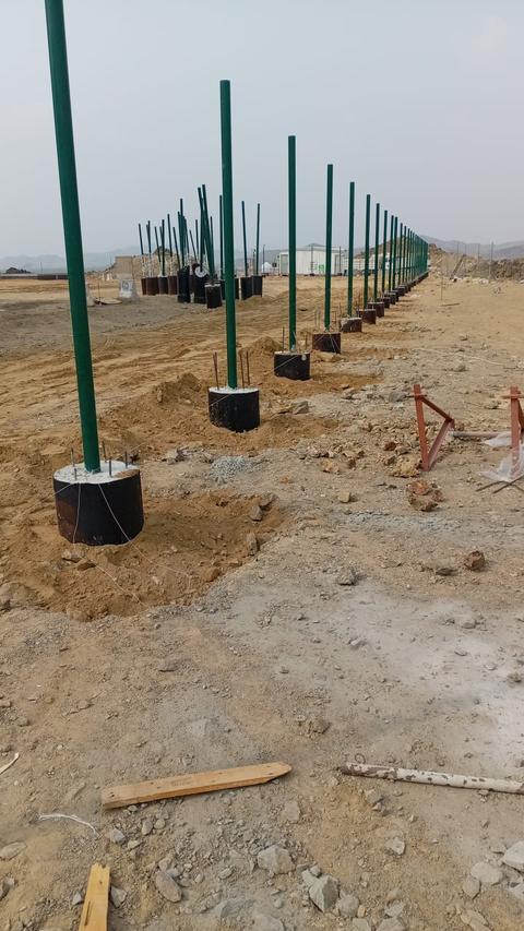 أعمدة حديد خضراء لشبوك ملعب مثبتة على قواعد خرسانية دائرية في موقع المشروع